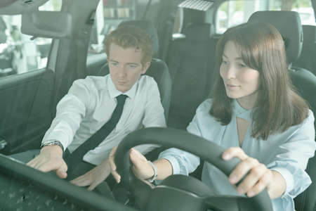 Young pretty brunette woman sitting in new car during test drive with manager
