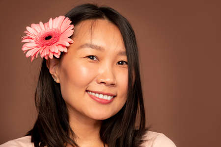 Happy young Asian woman with beautiful pink herbera in dark long hair