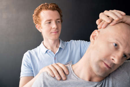 Young professional in physiotherapy standing behind bald mature patientの写真素材