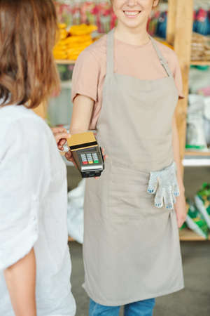 Contemporary female customer holding credit card over payment terminal