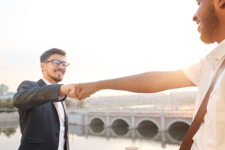 Close-up of multi-ethnic friends making fist bump while greeting each other against bridgeの写真素材