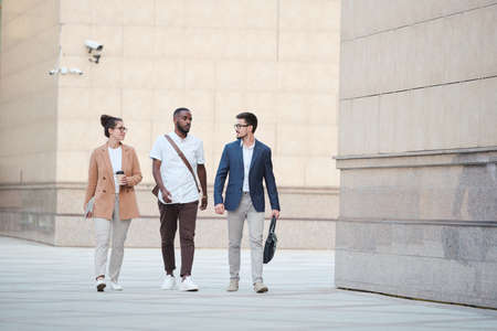 Confident young business specialists walking over business district and talking about project promotion on moveの写真素材