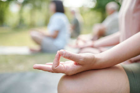 Close-up of unrecognizable woman touching fingers in mudra while meditating at group class outdoorsの写真素材