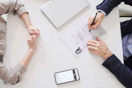 Directly frome above shot of unrecognizable woman sitting in front of man with CV paper having job interviewの写真素材