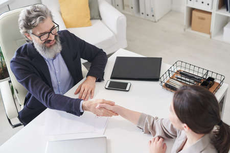 HIgh angle view shot of man and woman sitting at office desk in front of each other shaking hands...