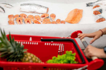 Unrecognizable woman with shopping cart choosing fresh salmon fish in modern store, copy spaceの写真素材