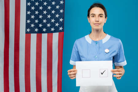 Young brunette chambermaid in blue uniform showing you her ballot paper