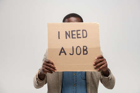 Young jobless man of African ethnicity hiding his face behind piece of cardboard