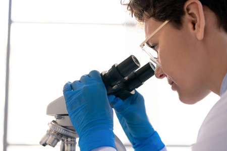 Head and gloved hands of young female scientist studying chemical reaction