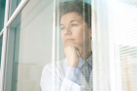 Young pensive female scientist or researcher in whitecoat keeping hand by chinの写真素材