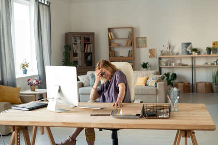 Mature blond cheerful female laughing in front of computer screen at home
