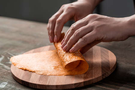 Close-up of unrecognizable woman rolling fruit leather on wooden board at table, homemade sweetsの写真素材