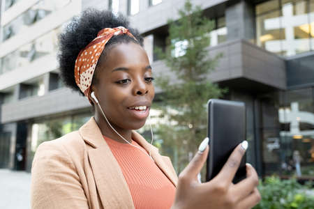 Happy young African businesswoman with earphones talking through video chat