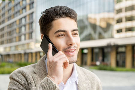 Happy young mixed-race businessman in formalwear talking to clients on the phoneの写真素材