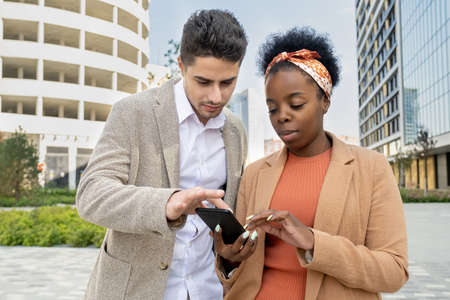 Young elegant businessman magnifying photo in smartphone of African colleagueの写真素材