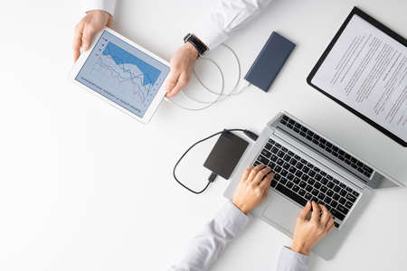 Top view of hands of two clinicians using mobile gadgets during work in hospital