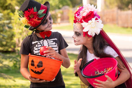 Cute halloweeen girl with dark long hair looking at friend basket with treatsの写真素材