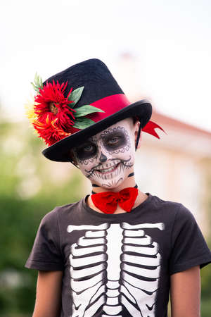 Cute smiling schoolboy with painted face in halloween costume of skeleton
