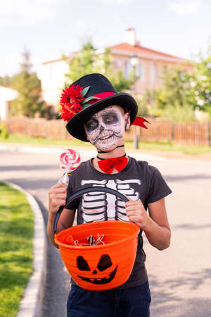 Cheerful boy with painted face in halloween t-shirt showing basket with sweetsの写真素材