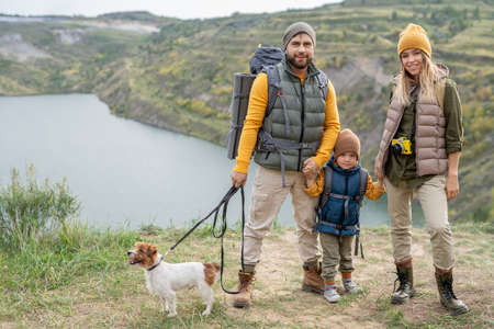 Happy young family of three in warm casualwear and their small dog on trip