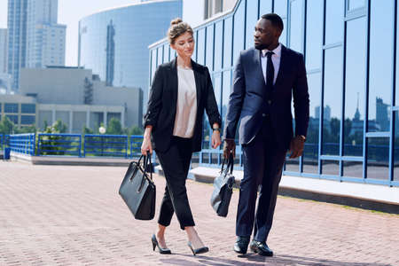 Young intercultural business partners in formalwear moving down sidewalkの写真素材