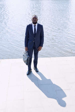 Young African businessman in formalwear holding black leather handbagの写真素材