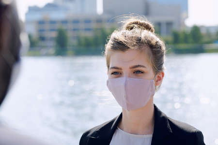 Young businesswoman in protective mask and formalwear looking at colleagueの写真素材