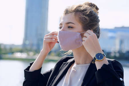 Young elegant businesswoman in formalwear putting on protective mask