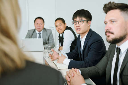 Young Asian businessman in formalwear questioning business coach at seminarの写真素材