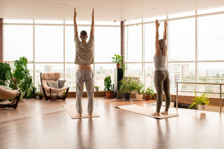 Back view of young active couple in sportswear standing on mats with raised armsの写真素材