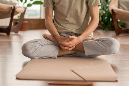 Arms and crossed legs of barefoot active young man sitting in pose of lotus
