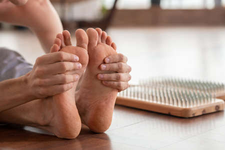 Barefoot man sitting on wooden floor and holding his feet during exerciseの写真素材