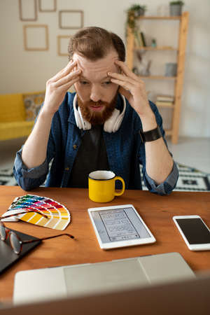 Young tired software developer touching forehead while bending over table