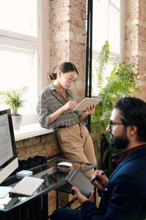 Young female designer using digital tablet while her colleague drawing sketchの写真素材
