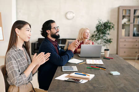 Three contemporary intercultural professionals clapping their hands after speech