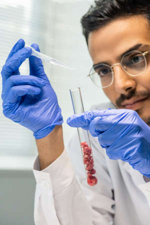 Gloved male worker of food quality control dropping liquid substance into flask