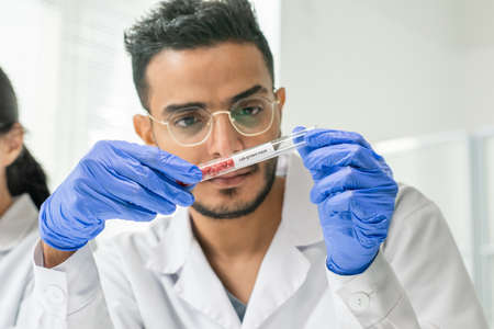 Gloved male worker of food quality control looking at tiny pieces of raw meatの写真素材