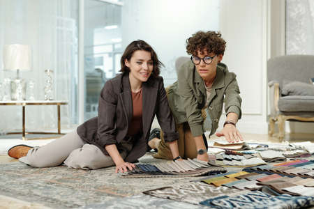 Young shop assistant of studio of interior design consulting female consumer