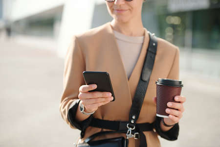 Hands of young businesswoman with glass of coffee scrolling through contactsの写真素材