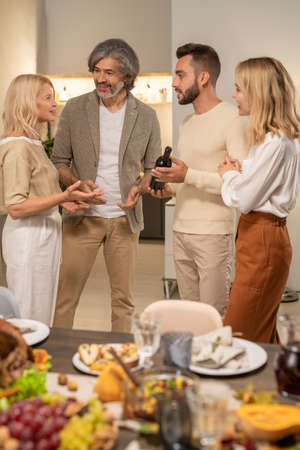 Four cheerful family members discussing wine held by young man in living-roomの写真素材