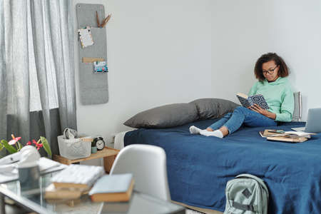 Young pretty diligent student with open book preparing home assignment