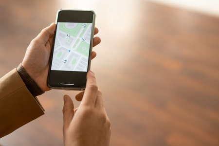 Hands of contemporary young man using smartphone to find out street or house