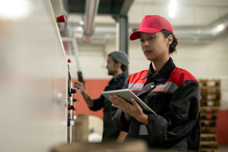 Young pretty female engineer with tablet entering data from control panelの写真素材