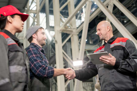 Bald mature foreman with digital tablet greeting his two young subordinates