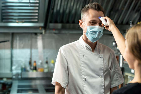 Contemporary chef in white uniform and protective mask looking at young womanの写真素材