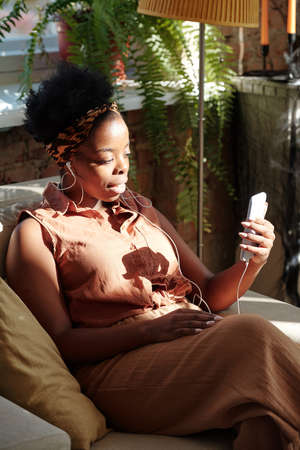 Young restful female of African ethnicity looking at smartphone screen