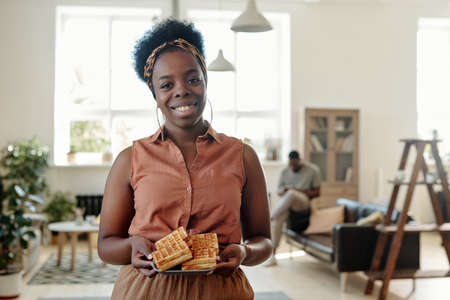 Young happy African female with homemade waffles standing against her husbandの写真素材