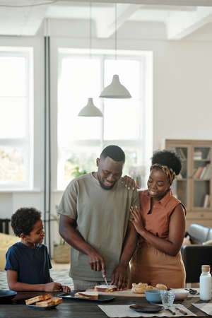 Young African man cutting bread while preparing sandwiches for his familyの写真素材