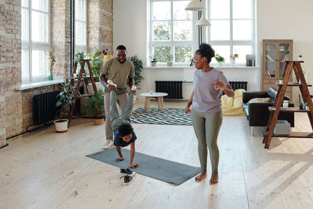 Young father holding legs of playful little son moving on hands on the floorの写真素材