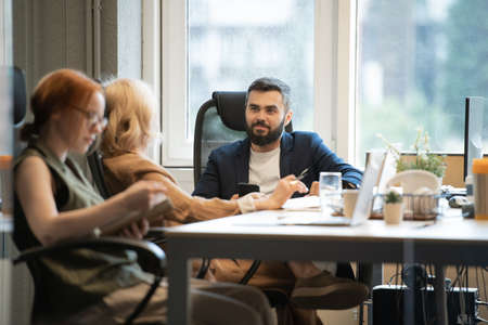 Young bearded businessman with smartphone talking to mature female colleagueの写真素材